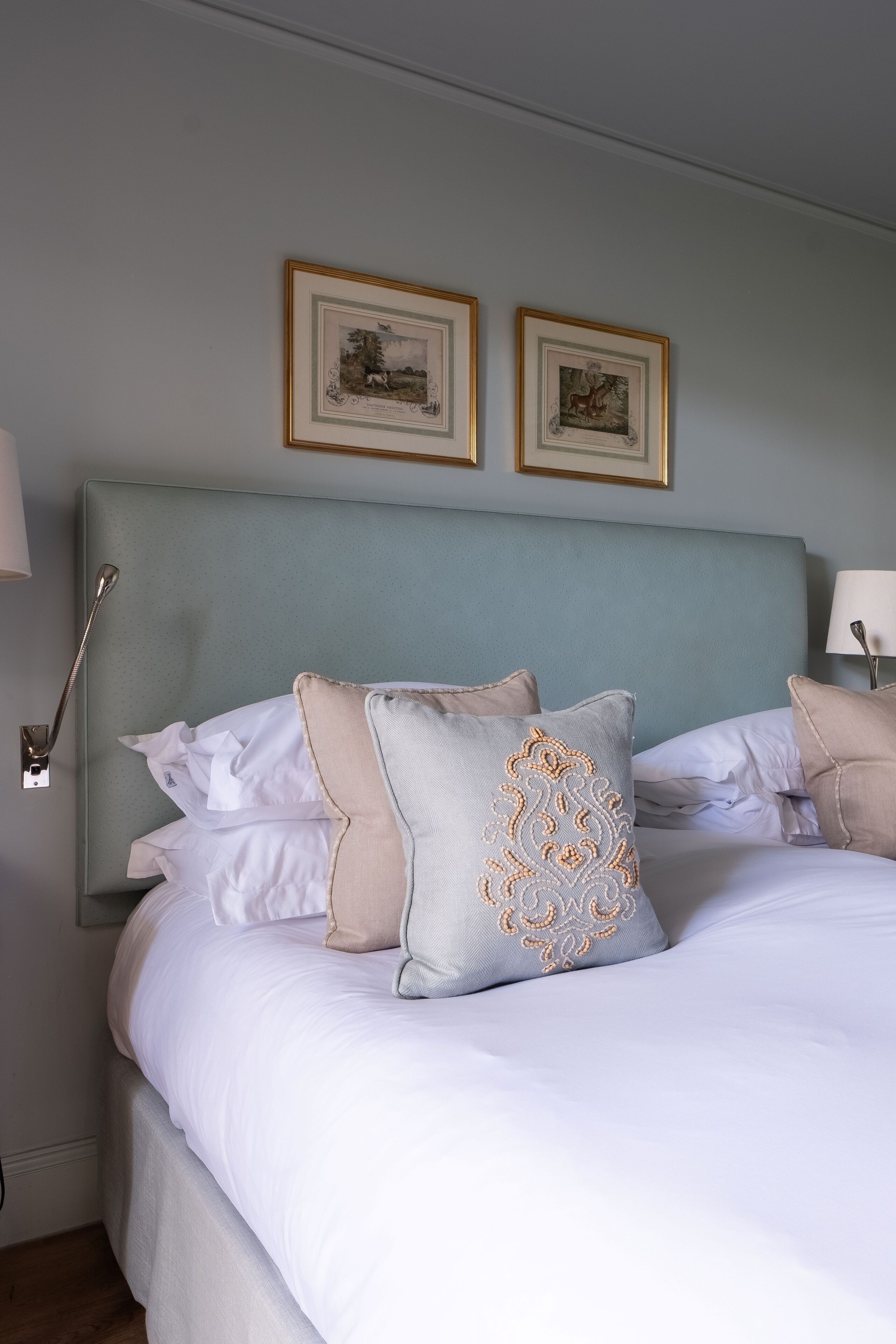 A neatly made bed with white linens and decorative pillows, a headboard, and two framed pictures on the wall.