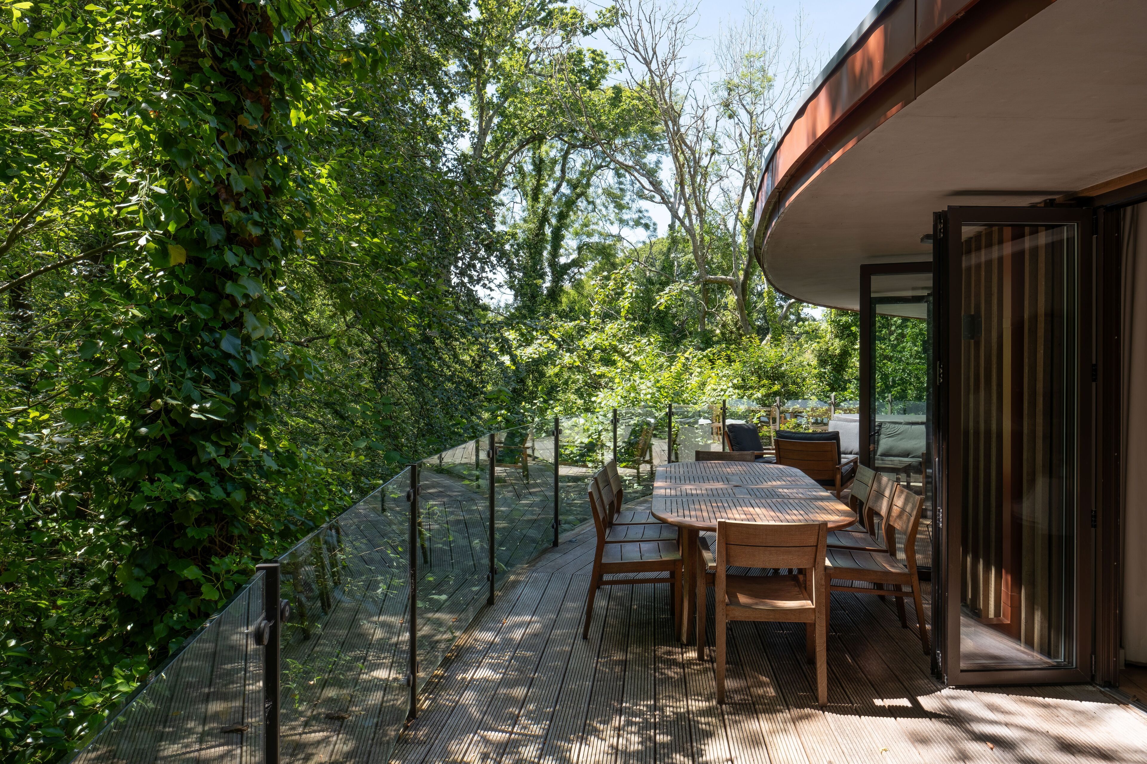 An outdoor patio with a table and chairs, surrounded by a metal fence and lush greenery.