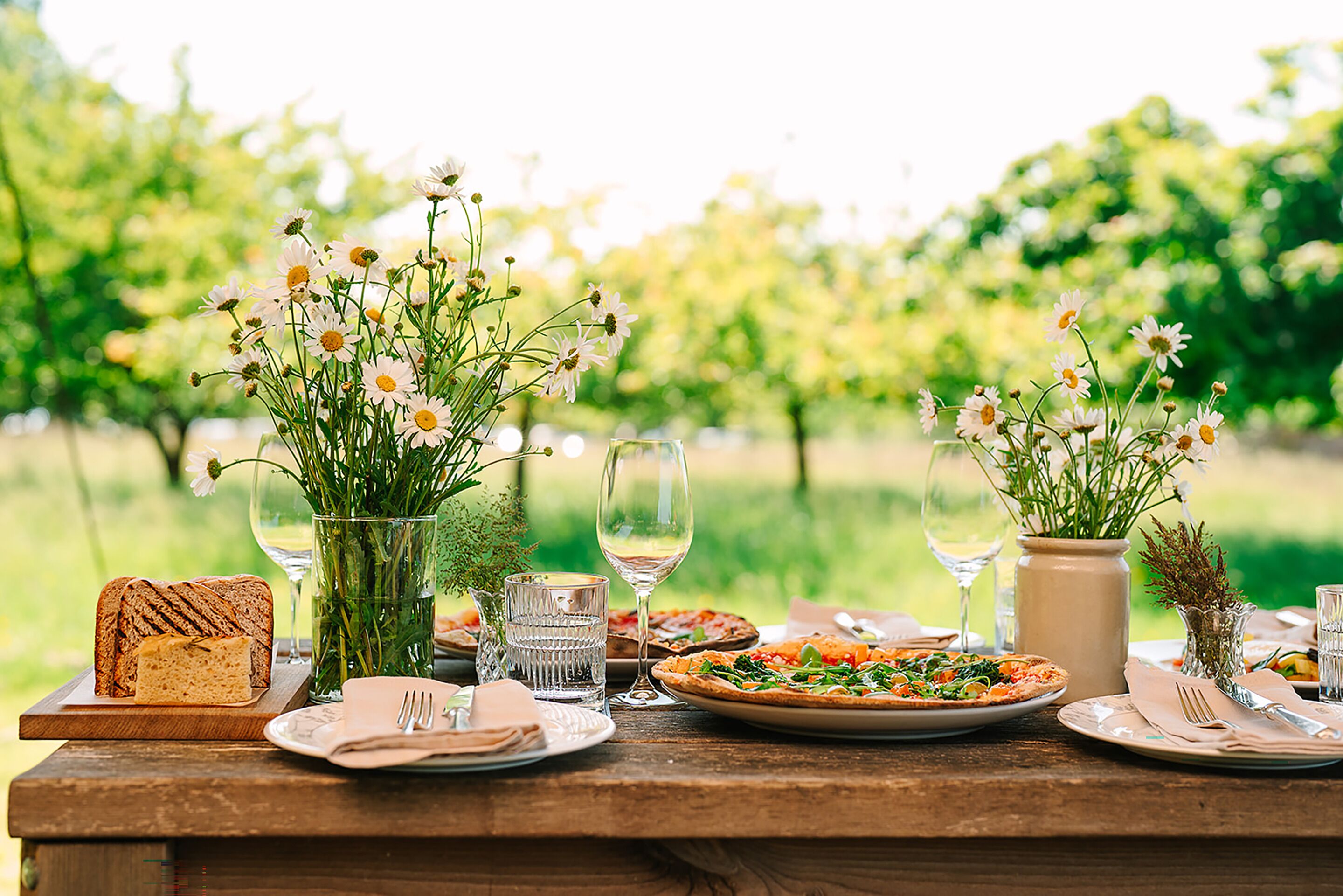 Ett picknickbord med tallrikar fulla av mat, glas med vatten och en vas med blommor.