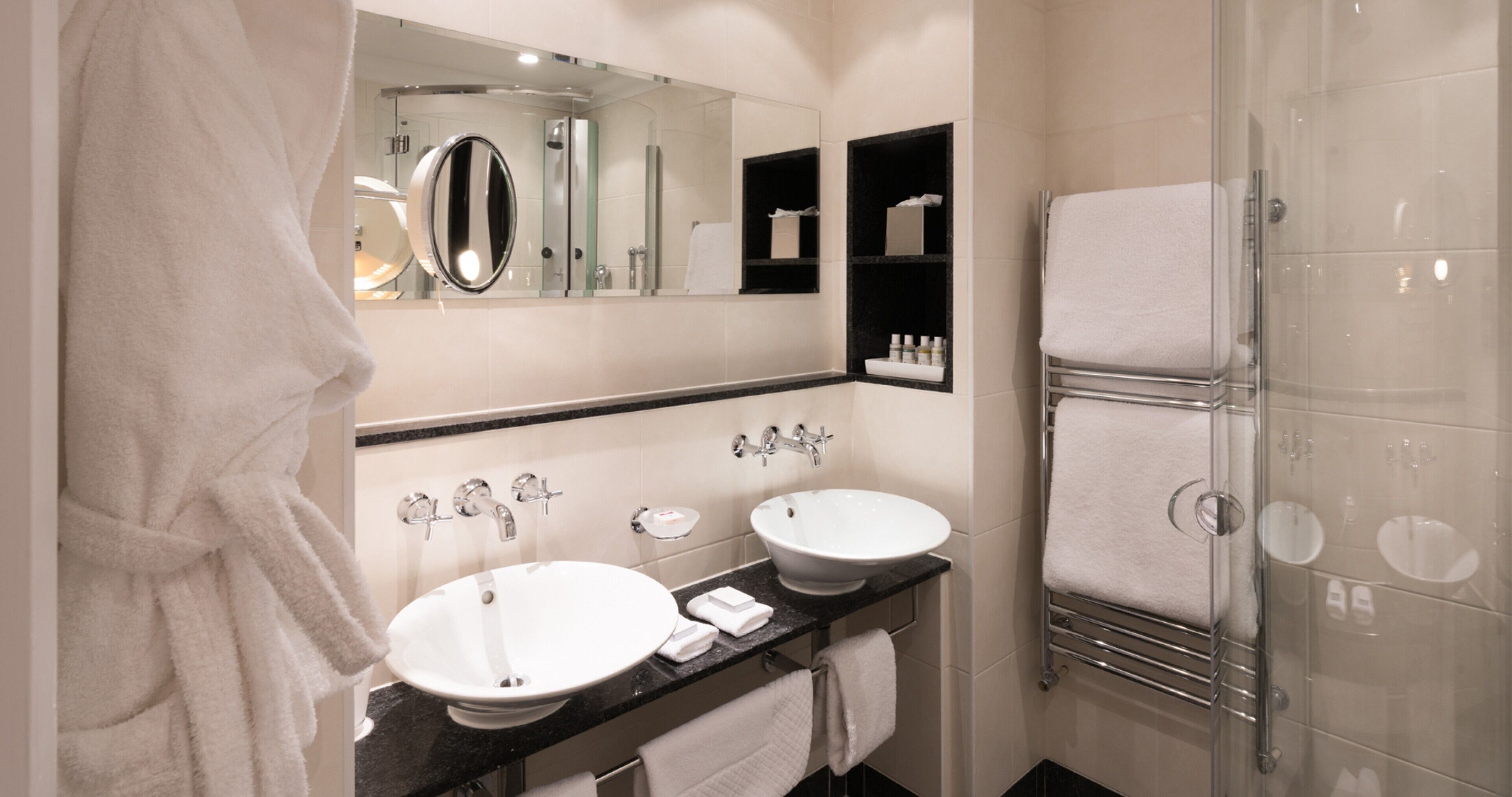 A modern bathroom with two sinks, a large mirror, and a glass shower enclosure.