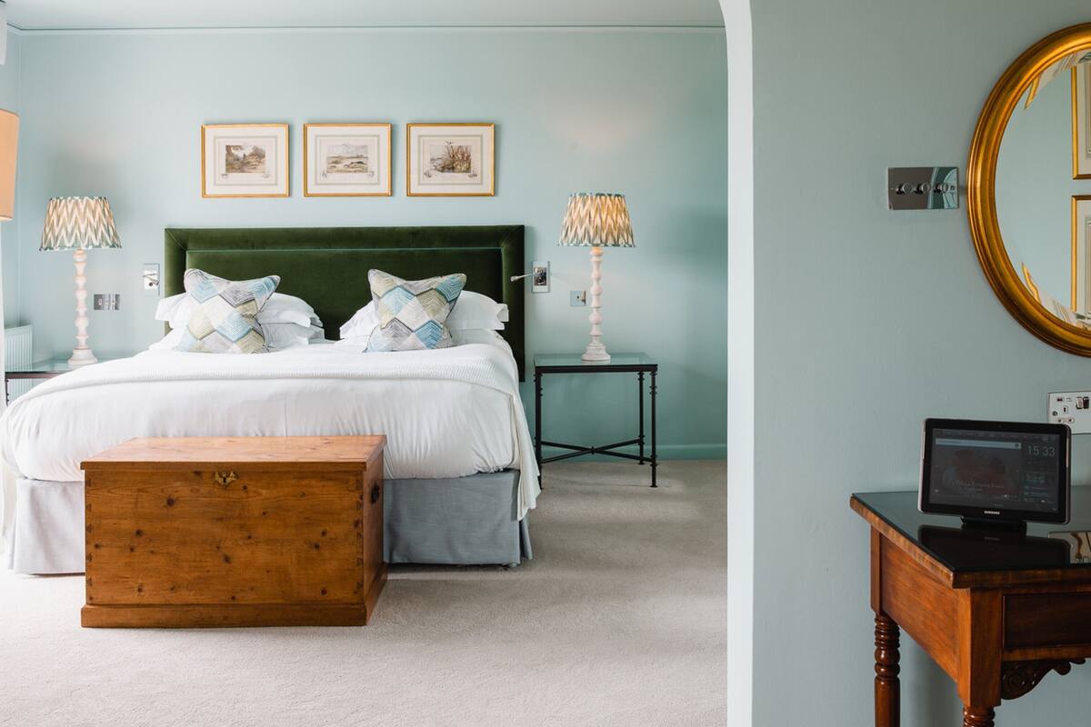 A bedroom with a bed, bedside tables, a wooden chest, a mirror, and a television.