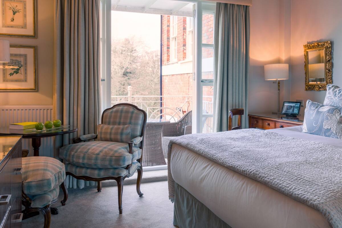 A hotel room with a bed, a chair, a table with a lamp, and a view of the outside.