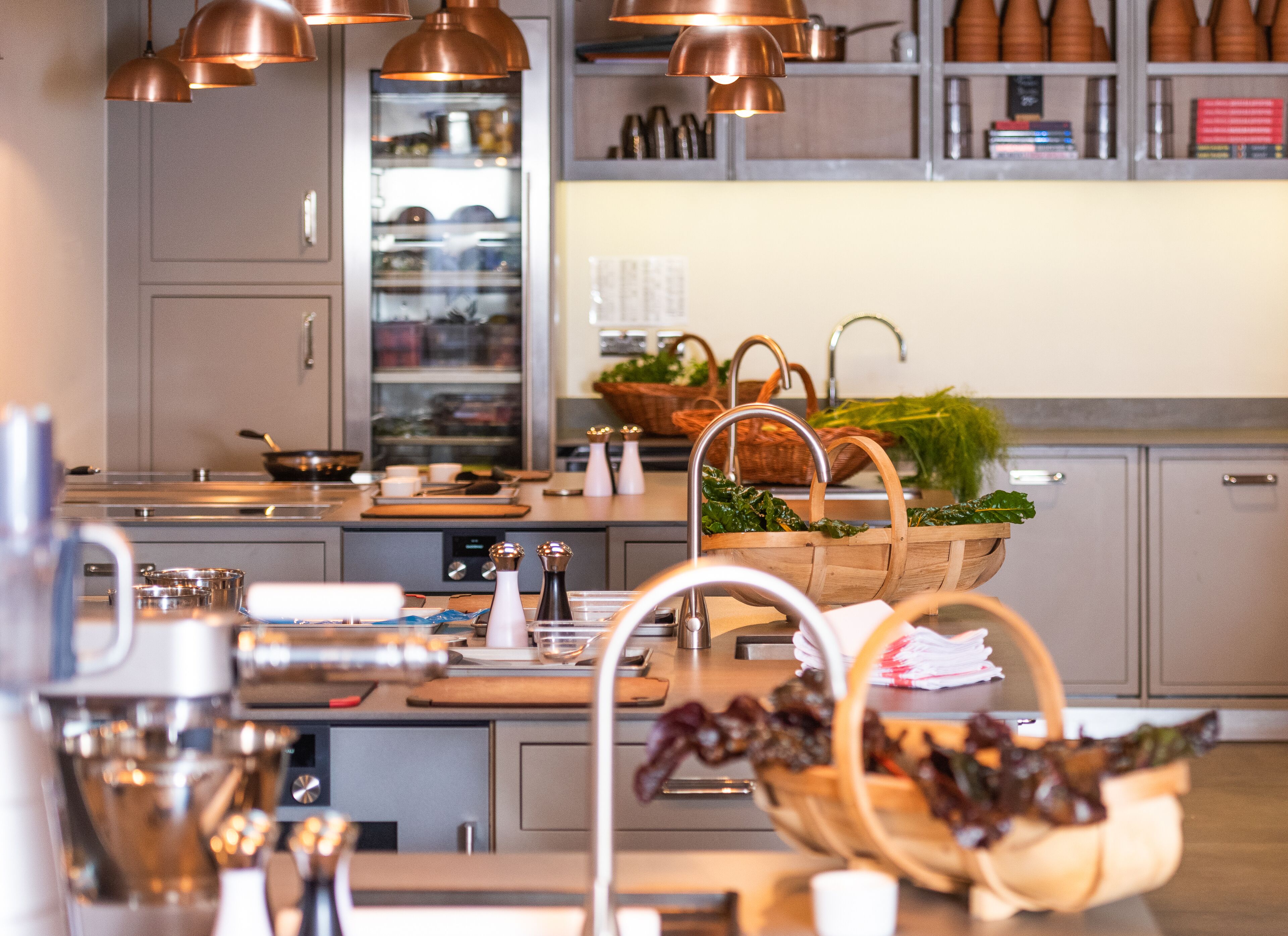 Una cocina moderna con lámparas colgantes de cobre, electrodomésticos de acero inoxidable y cestas de madera llenas de verduras frescas.