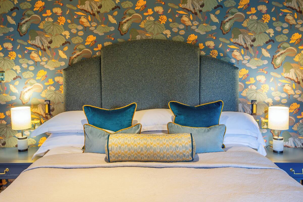 Una cama con cabecera, almohadas y mesitas de noche con lámparas.