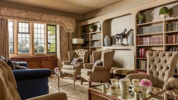 A classic library room with leather armchairs, a blue sofa, and a bookshelf filled with books and decorative items.