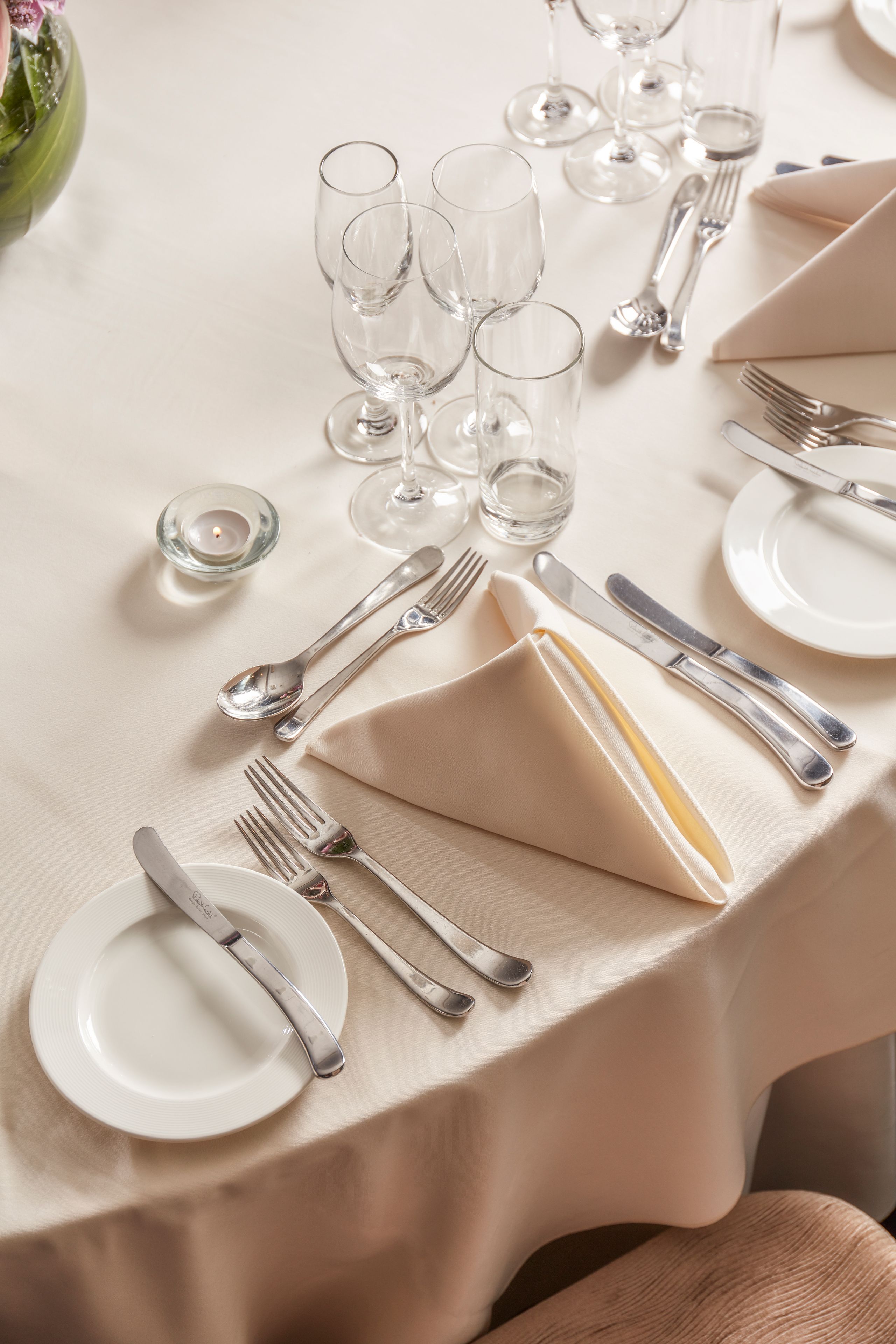 Mesa de jantar bem posta, com pratos, talheres e copos.