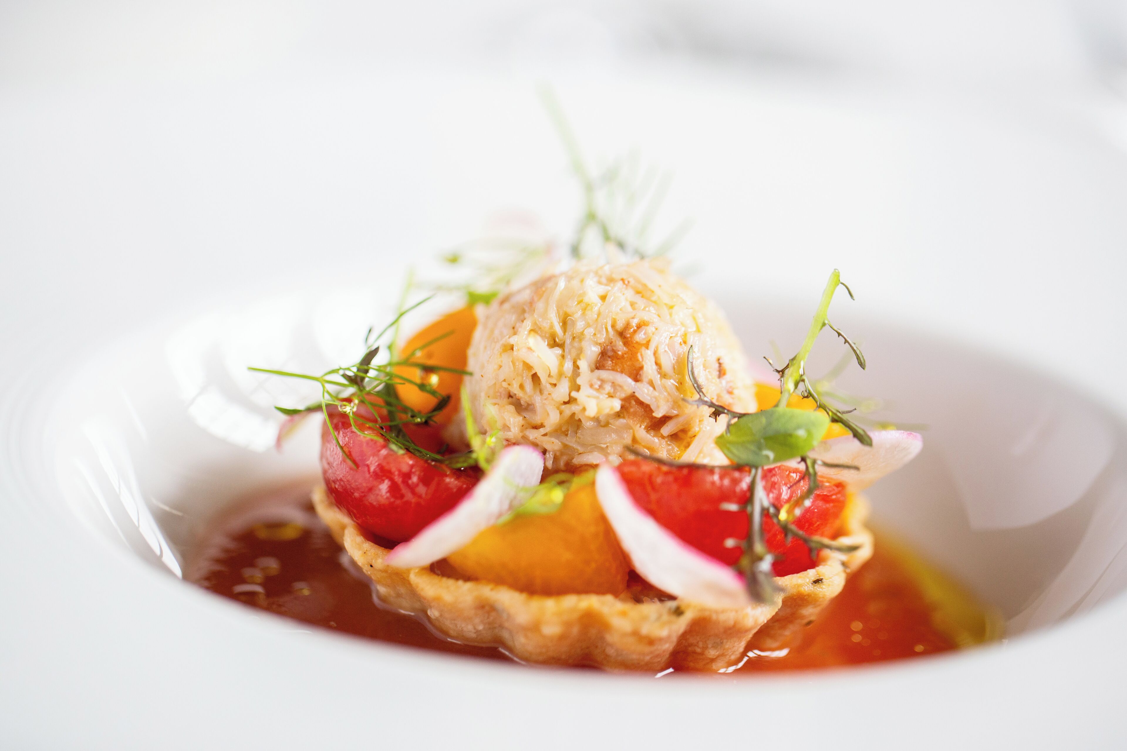 A dessert with a scoop of ice cream on top of a tart, surrounded by fruit and garnished with herbs.