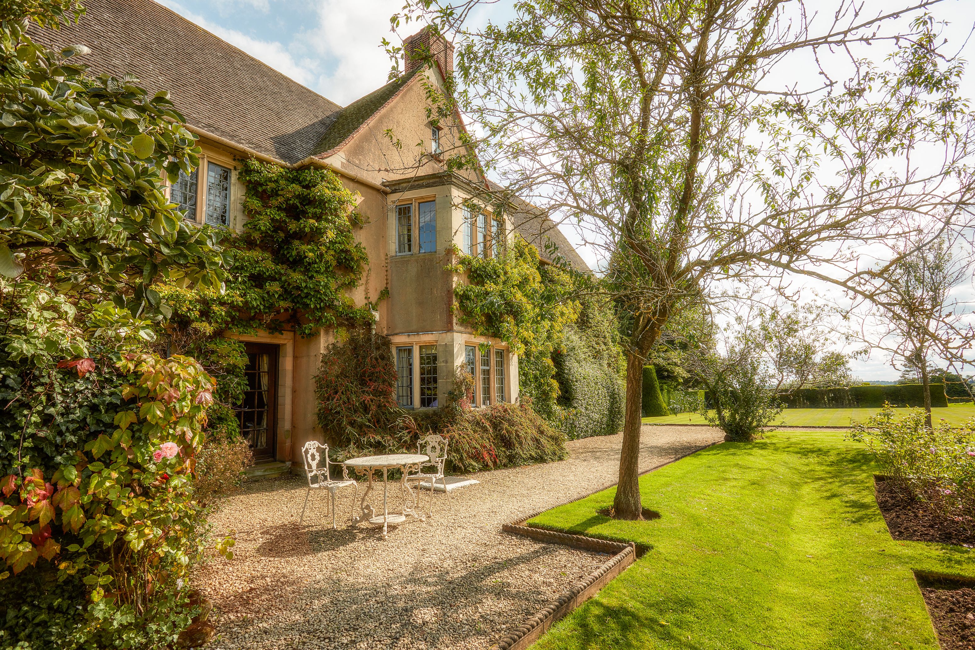 Ein Haus mit Garten, Kiesterrasse und einem weißen Tisch und Stühlen im Freien.