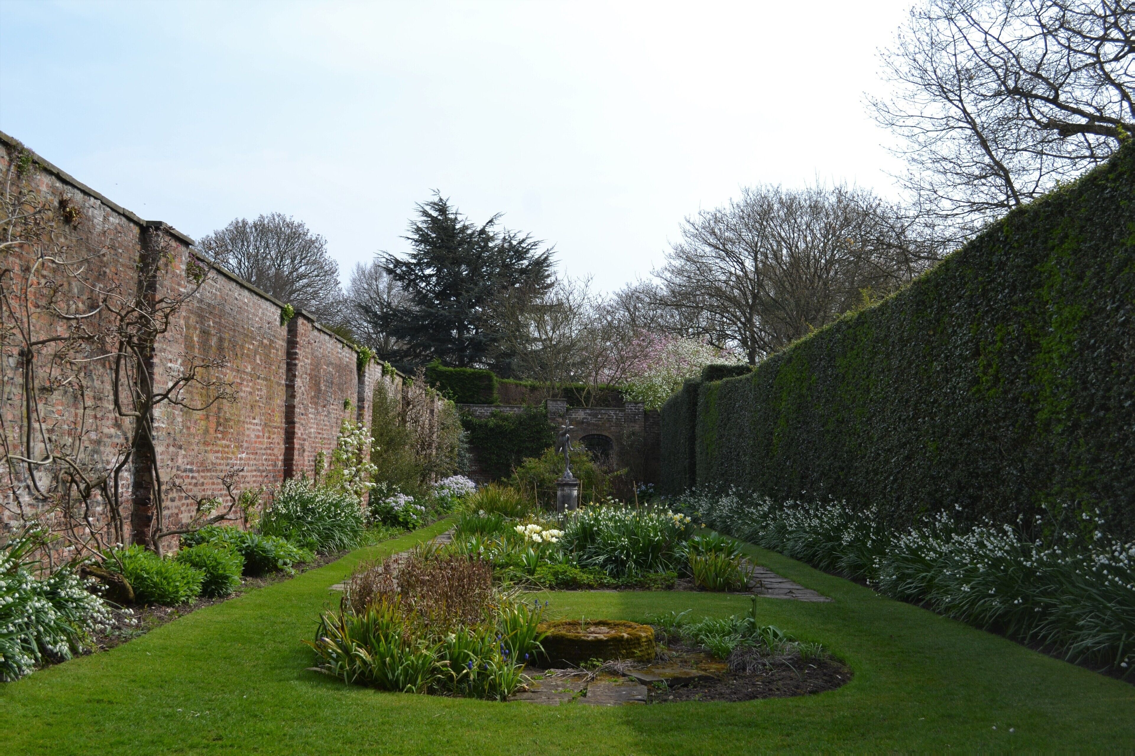 A garden with a brick wall, a stone bridge, and various plants.