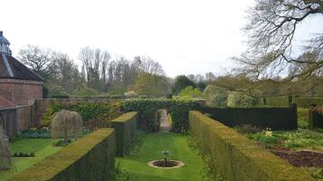 A formal garden with a central fountain, neatly trimmed hedges, and a brick building with a dome.