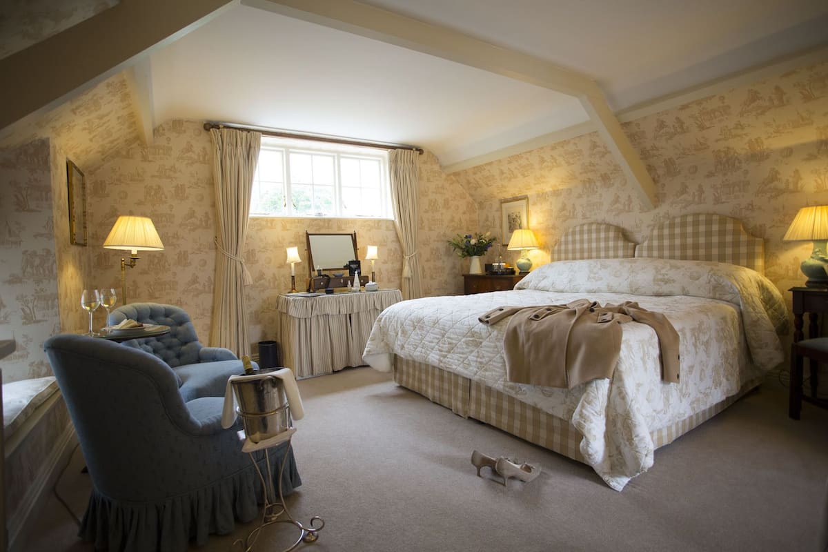 A bedroom with a large bed, a chair, a vanity with a mirror, and a window with curtains.