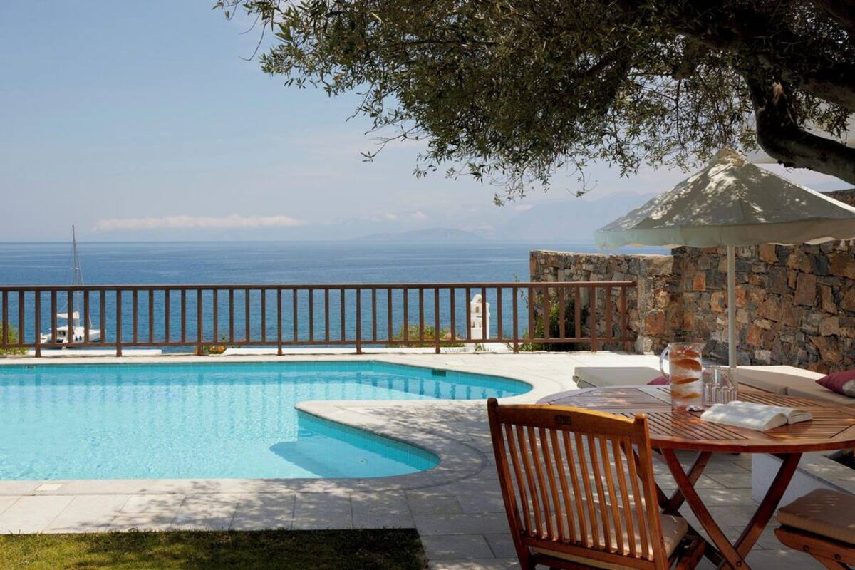Ein Schwimmbecken mit einer Steinmauer, einer Holzterrasse und Blick aufs Meer.