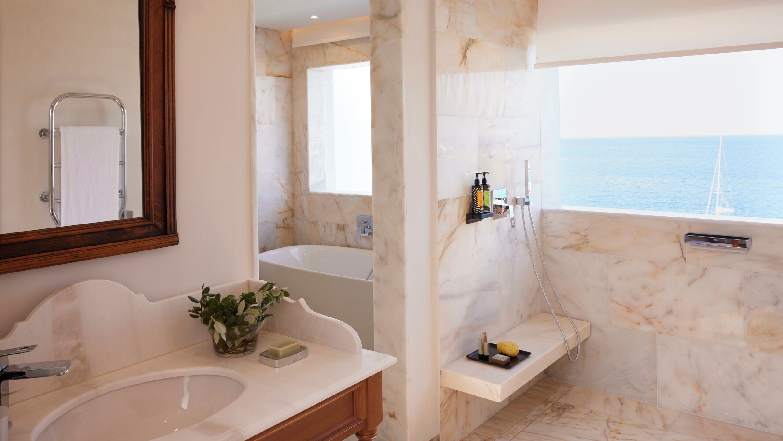 A bathroom with a bathtub, a sink, a mirror, and a shower area with a view of the sea.