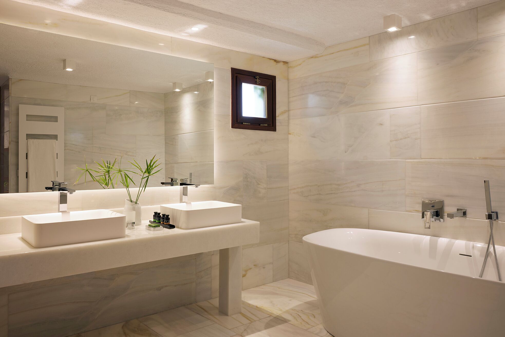 Een moderne badkamer met twee wastafels, een ruim bad en een spiegel met een klein raam.