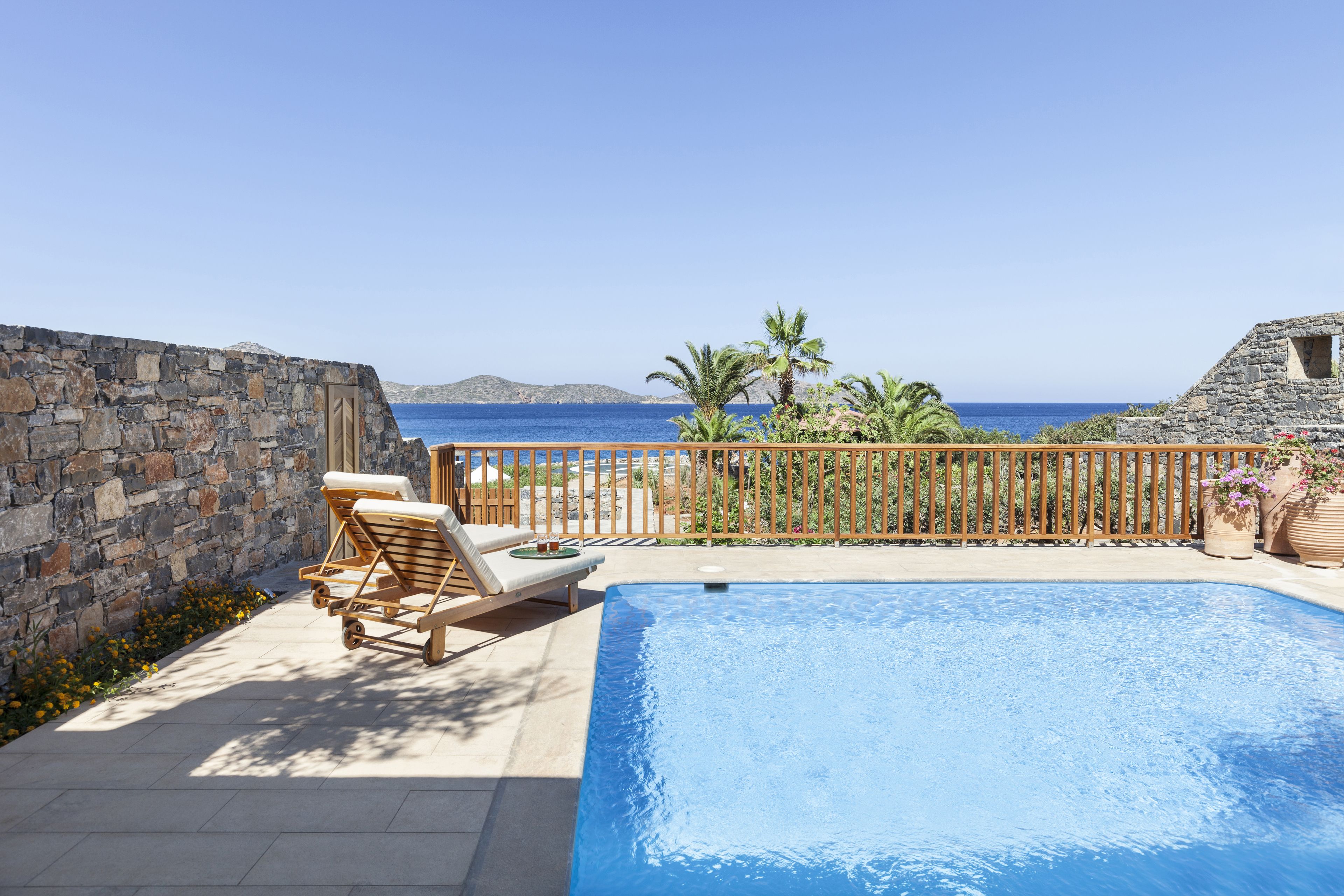 Una piscina con sillas de descanso, un muro de piedra y vista al mar.