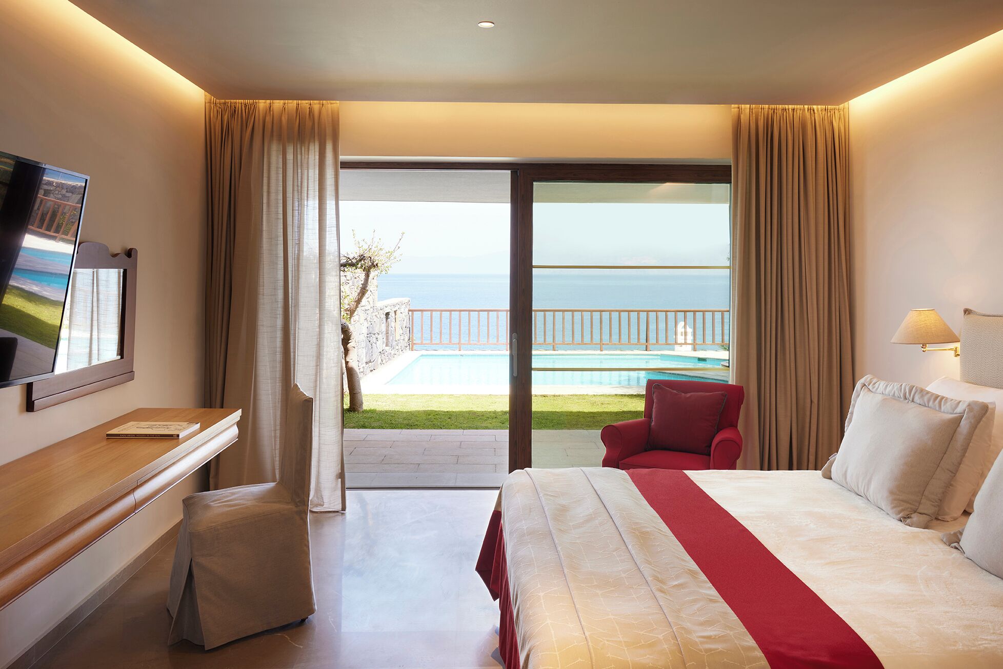 A hotel room with a bed, a desk, a TV, and a view of the ocean.