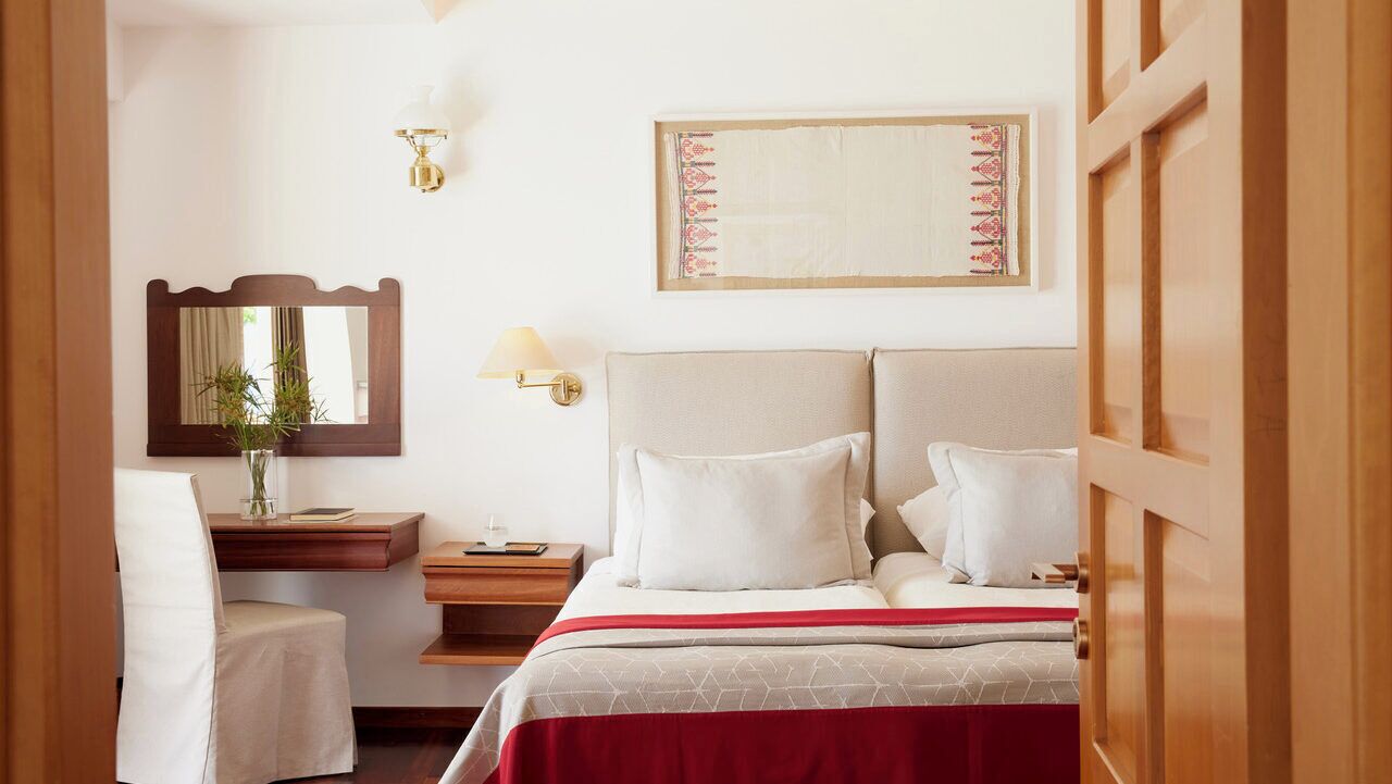 Habitación de hotel con cama, mesita de noche, lámpara, espejo y un cuadro en la pared.