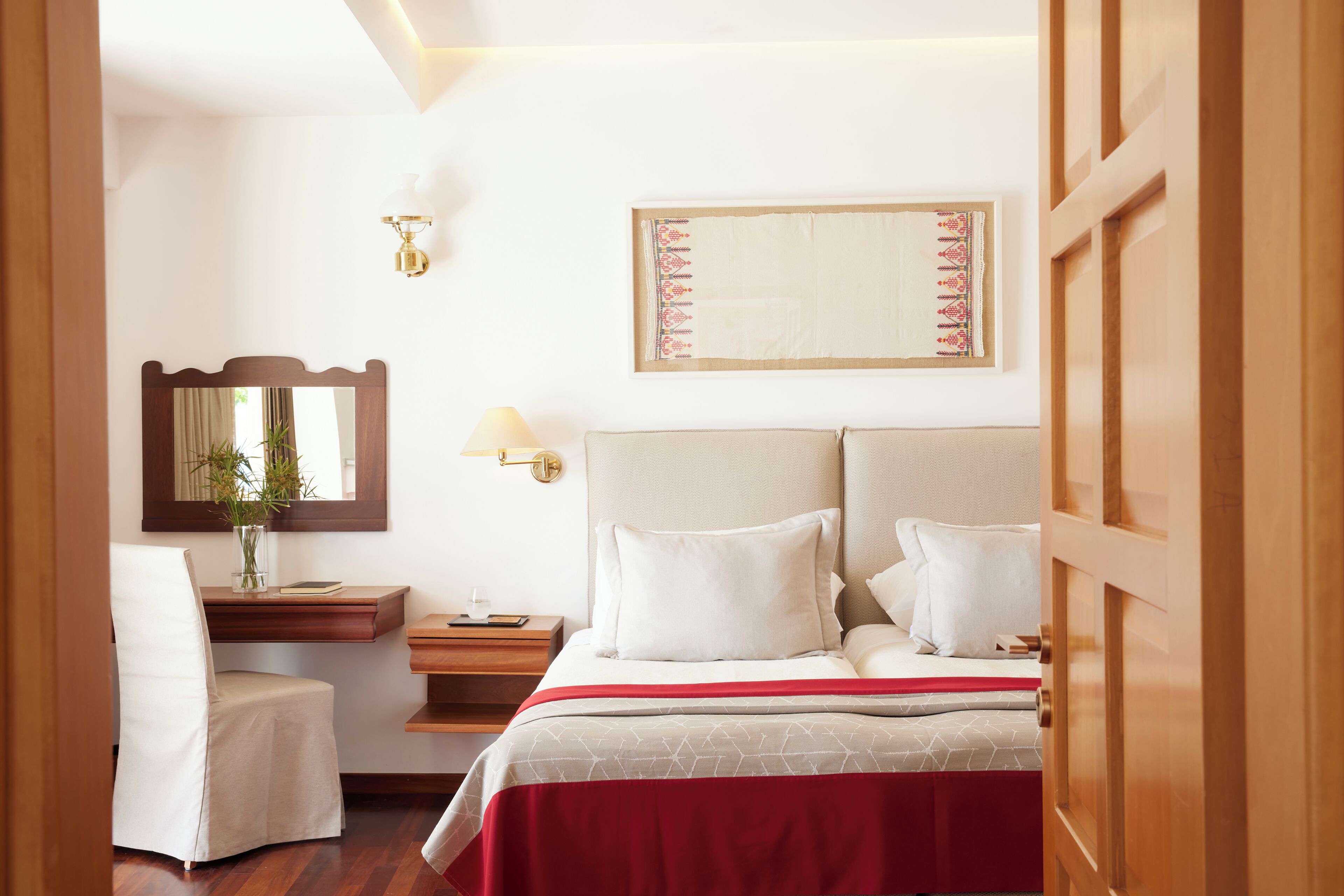A hotel room with a bed, a chair, a nightstand, a lamp, a mirror, and a wall-mounted artwork.