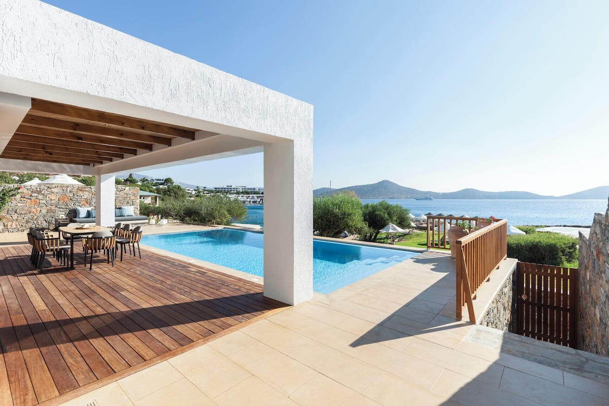 Ein Poolbereich mit Holzterrasse, Sitzgelegenheiten im Freien und Blick aufs Meer.
