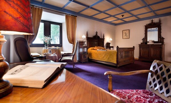 A hotel room with a large bed, a desk with a book, a chair, a wooden dresser, and a window with curtains. - Château de Coudrée (Sciez)