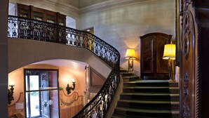 Un magnifique escalier orné de balustrades travaillées, surmonté d’un lustre et agrémenté de lampes, menant à l’étage supérieur.