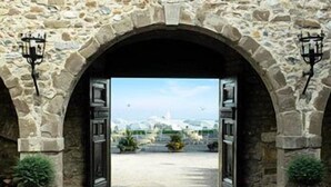 Une entrée ornée d’arcs en pierre, d’où l’on aperçoit un bâtiment au loin.