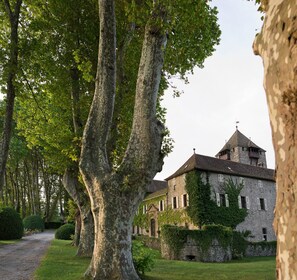 A stone building with a tower, surrounded by trees and a gravel path. - Château de Coudrée (Sciez)