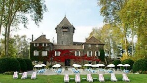 Un grand bâtiment en pierre, doté d’une tour, entouré d’une pelouse bien entretenue et bordé d’une étendue d’eau.