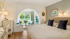 Une chambre avec un grand lit, un bureau, une chaise et une vue sur la verdure environnante.