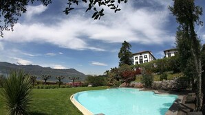 Una piscina con bordo curvo, circondata da un prato e da un solarium in pietra. Si notano lettini e un muro in pietra sullo sfondo.