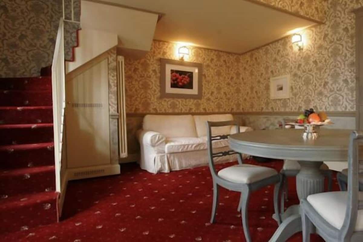 A room with a red carpet, a white sofa, a dining table with chairs, and a staircase.