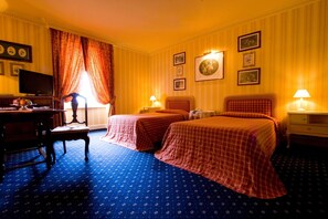 A hotel room with two beds, a desk, a television, and a window with curtains.
