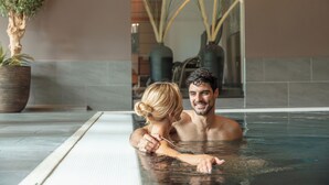 A couple in a hot tub with a potted plant and vases in the background.