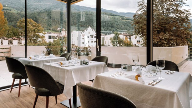A restaurant with tables set for dining, large windows offering a view of a mountainous landscape.