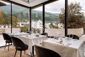 A restaurant with tables set for dining, large windows offering a view of a mountainous landscape. - Dominik Alpine City Wellness Hotel (Bressanone)