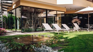 A modern outdoor lounge area with glass walls, a small water feature, and sun loungers.
