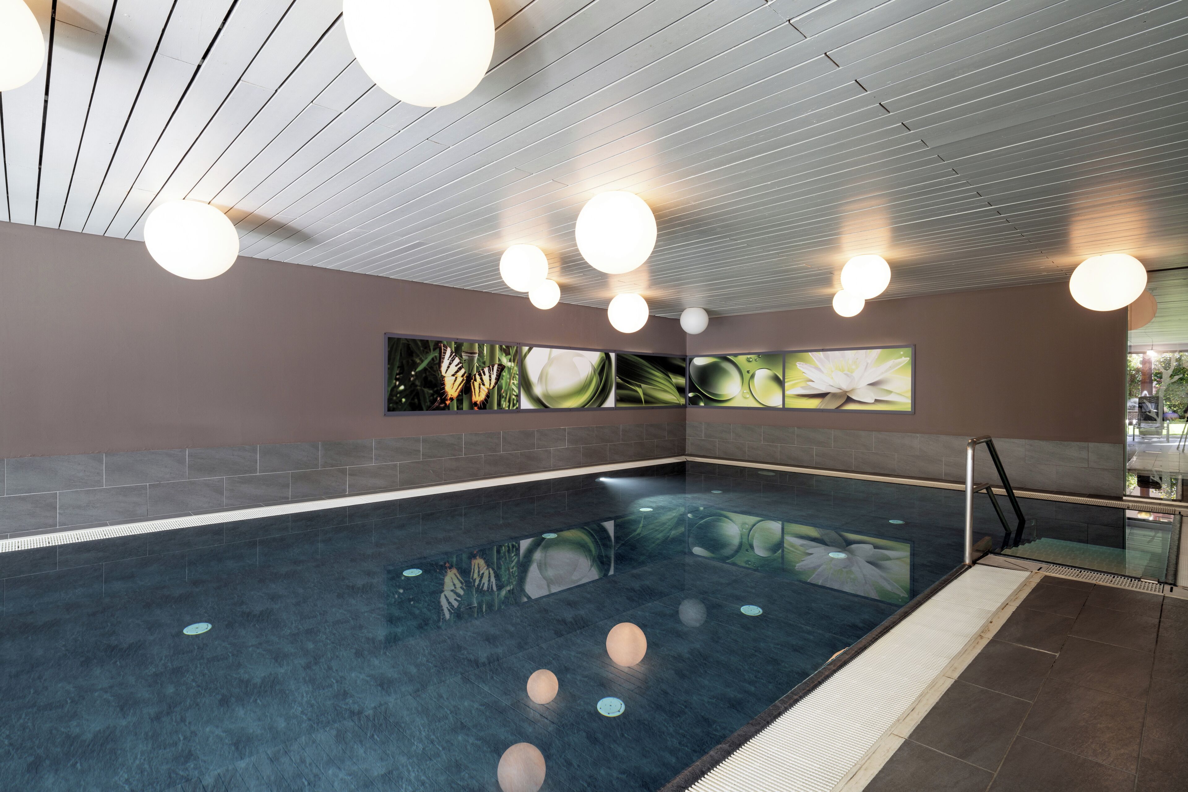 Uma grande piscina interior com chão em mosaico, rodeada por paredes decoradas com obras de arte.
