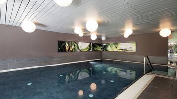Uma grande piscina interior com chão em mosaico, rodeada por paredes decoradas com obras de arte.