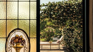 A stained glass window with a floral design, a brick pathway, and a view of a garden with a staircase.