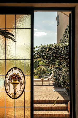 A stained glass window with a floral design, a brick pathway, and a view of a garden with a staircase.