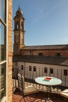 Un balcone con tavolo e sedia, affaccia su un edificio con un campanile e un tetto in tegole.