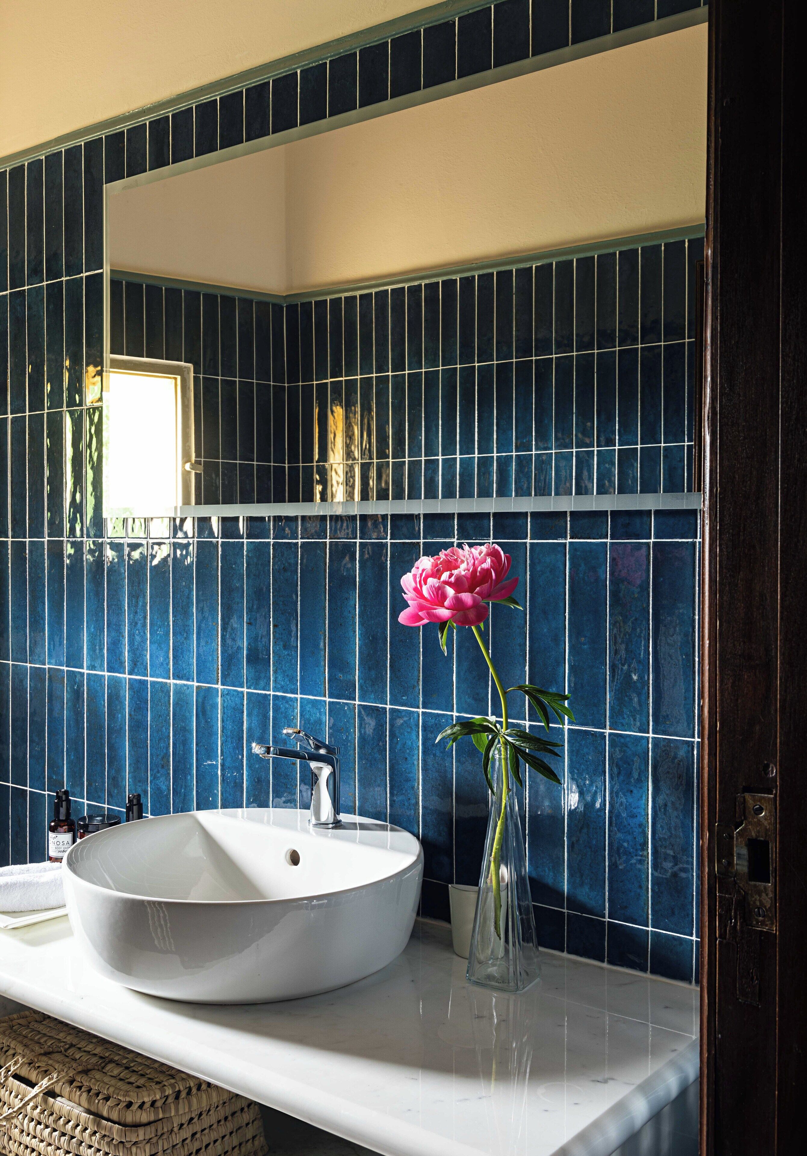 Un baño con un lavabo blanco, un espejo y un florero con una flor rosa.