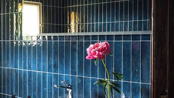 Un baño con un lavabo blanco, un espejo y un florero con una flor rosa.