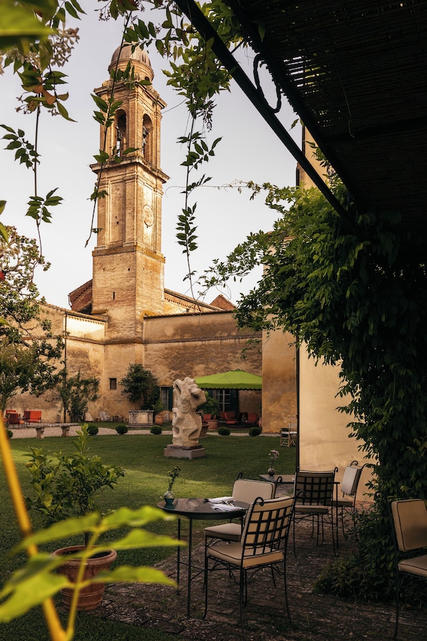 A courtyard with a stone building featuring a bell tower, outdoor seating, and greenery.