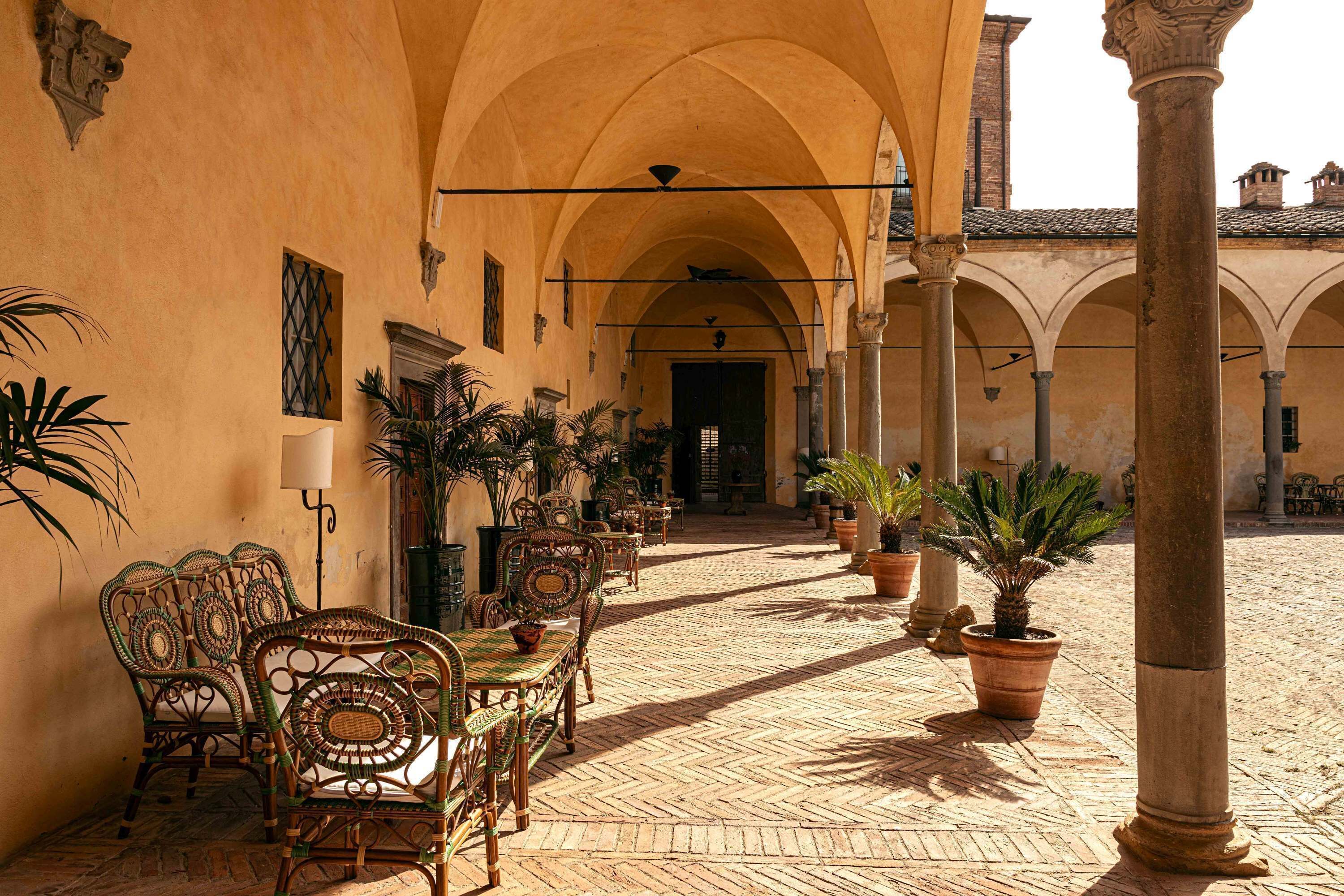 An outdoor courtyard with a tiled floor, arched ceilings, and potted plants.