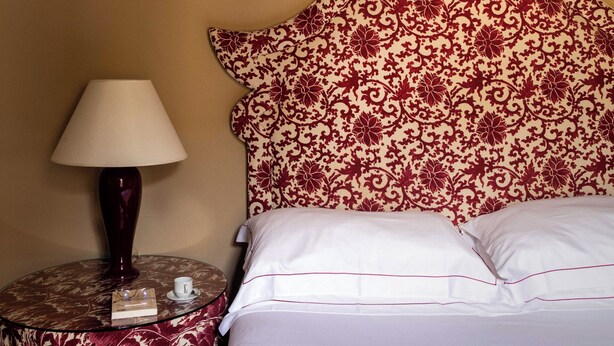 Un lit avec une literie blanche et une tête de lit décorative ornée d’un motif floral.