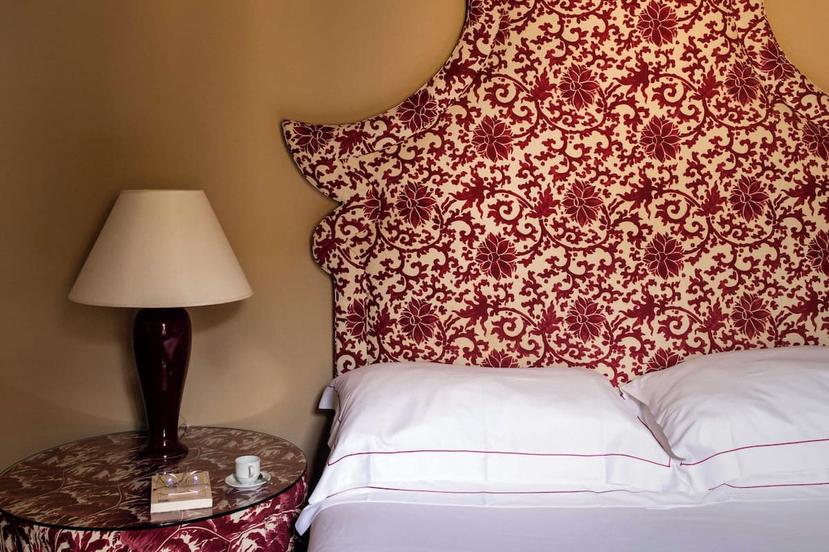 Una cama con ropa blanca y un cabecero decorativo con estampado floral.