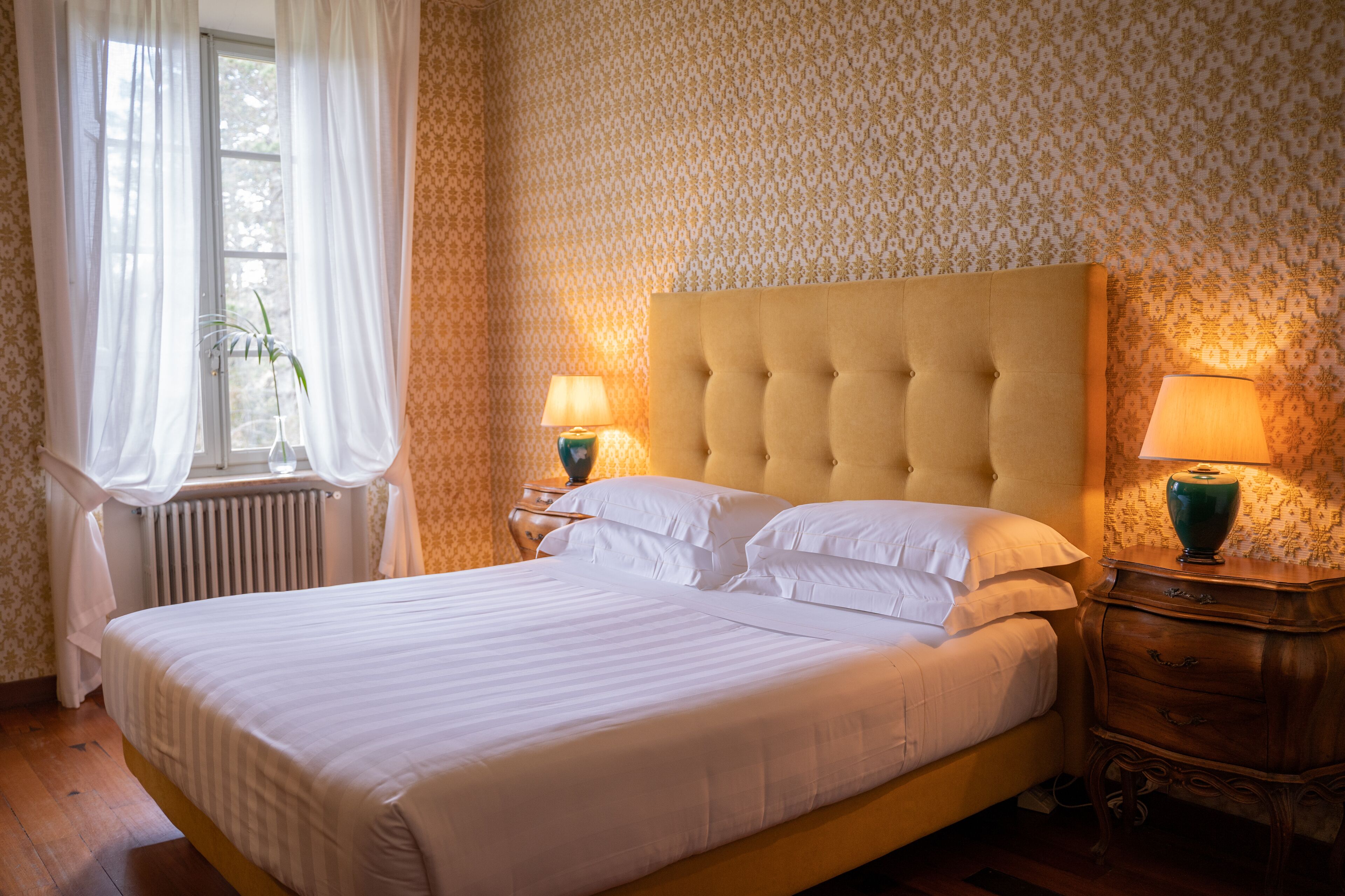 A neatly made bed with white linens, two bedside tables with lamps, and a radiator.