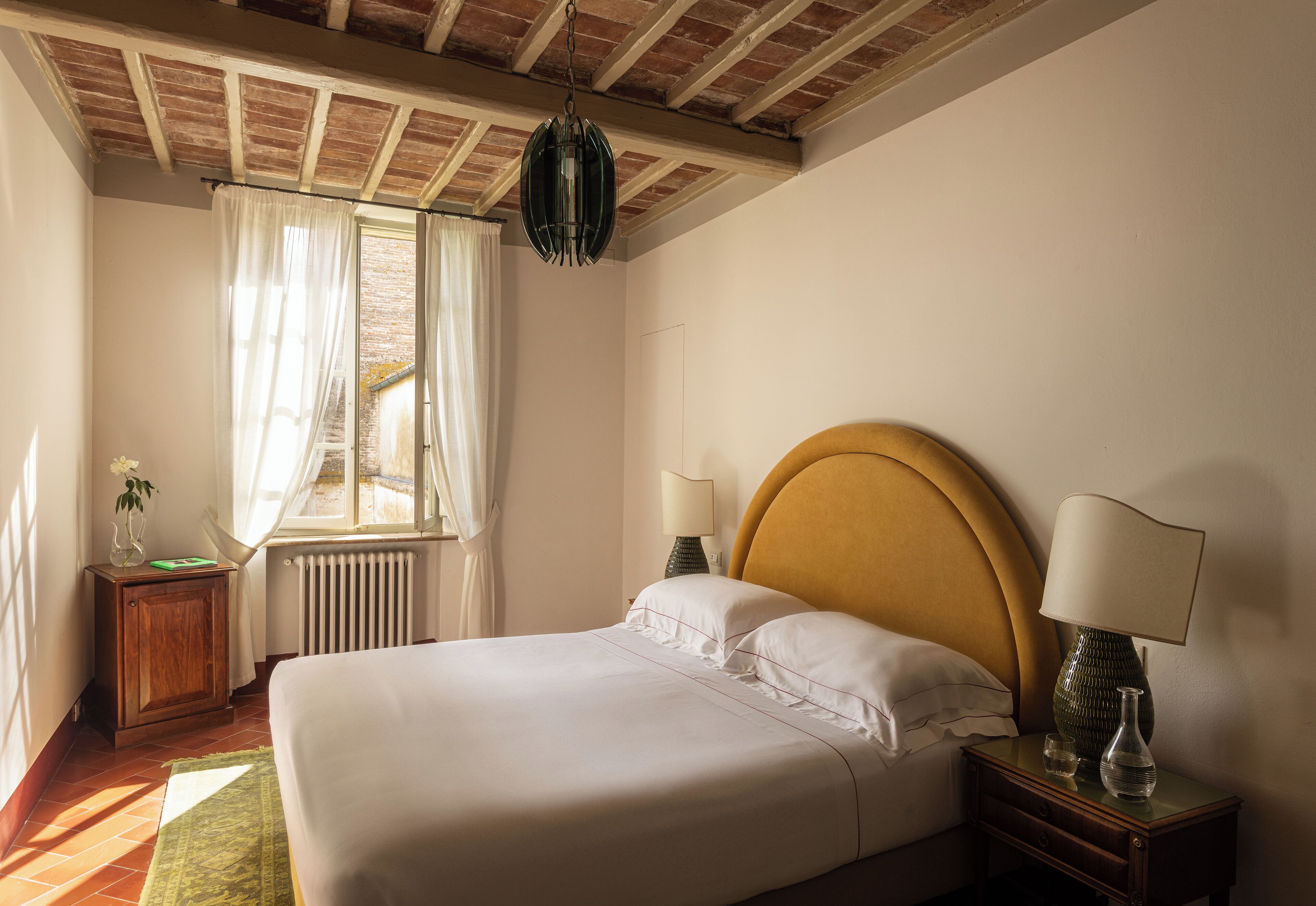 Una cama bien hecha con sábanas blancas, cabecera de madera y dos lámparas de noche.