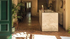 An arched hallway with a marble reception desk, potted plants, and a staircase in the background.